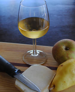 Glass of white wine with fruit and cheese plate.